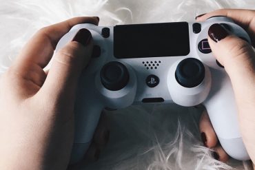 Weibliche Hände mit lackierten Fingernägeln halten einen PlayStation-Controller.