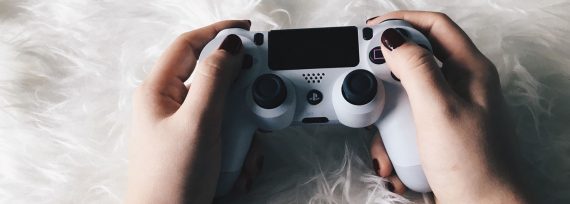 Weibliche Hände mit lackierten Fingernägeln halten einen PlayStation-Controller.